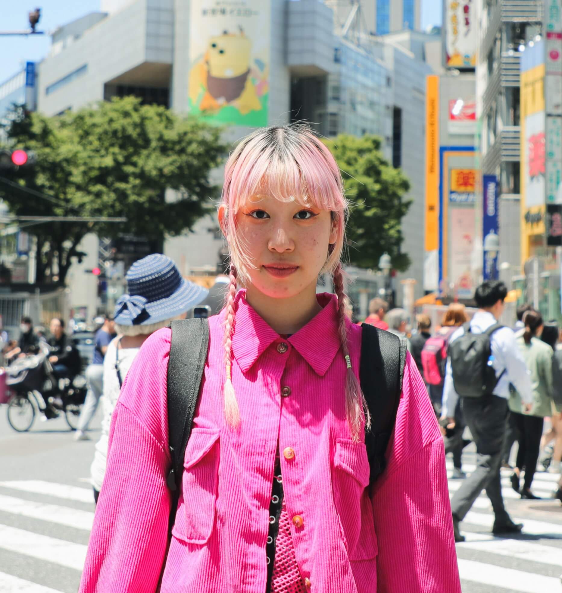 Young woman with pink hair and wearing a pink shirt stands outside on a busy city street