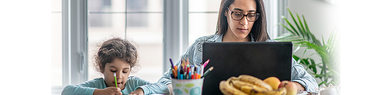 Worman sitting in home office working on laptop while a child is coloring sitting next to her