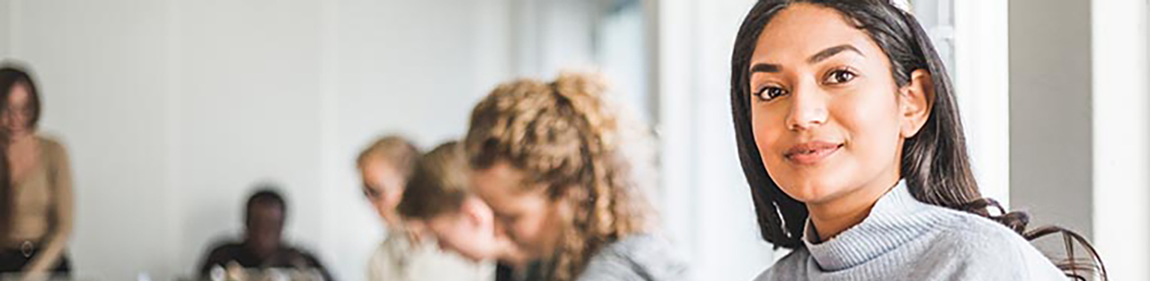 Woman with dark hair and gray sweater sitting in classroom